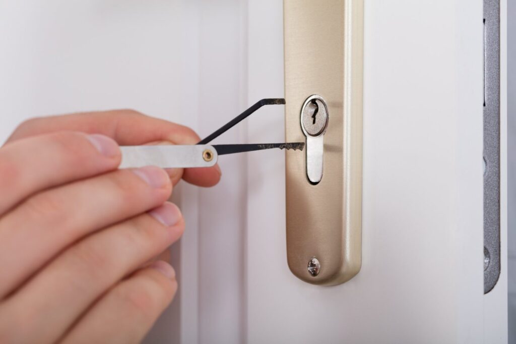 Hand using a lock pick set on the cylinder of a white door with a brushed metal handle plate