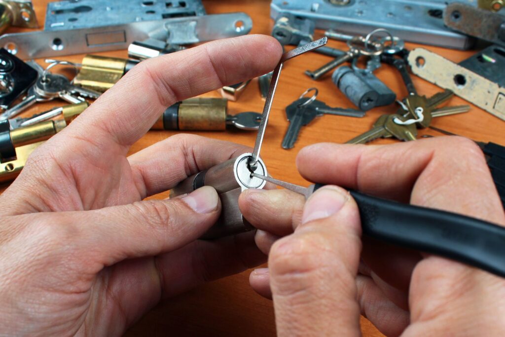 Locksmith working two slim tools into a lock cylinder keyway at a bench covered with keys and lock parts