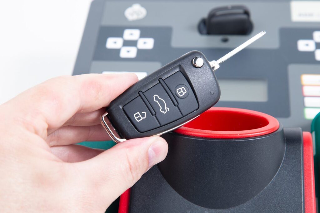 Flip car key with remote buttons held in front of a key cutting and programming machine
