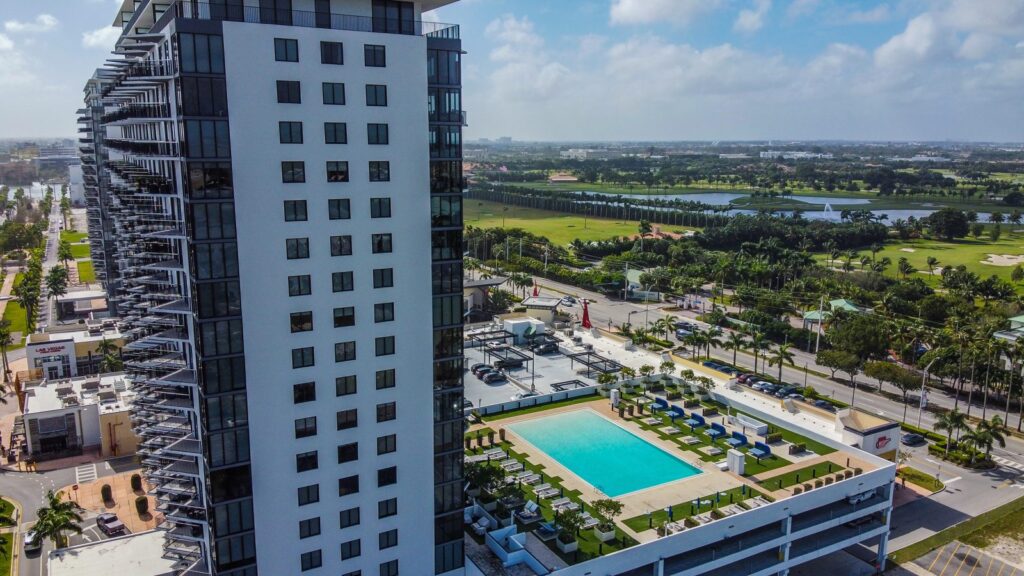 Aerial view of a Doral apartment tower with rooftop pool beside a golf course