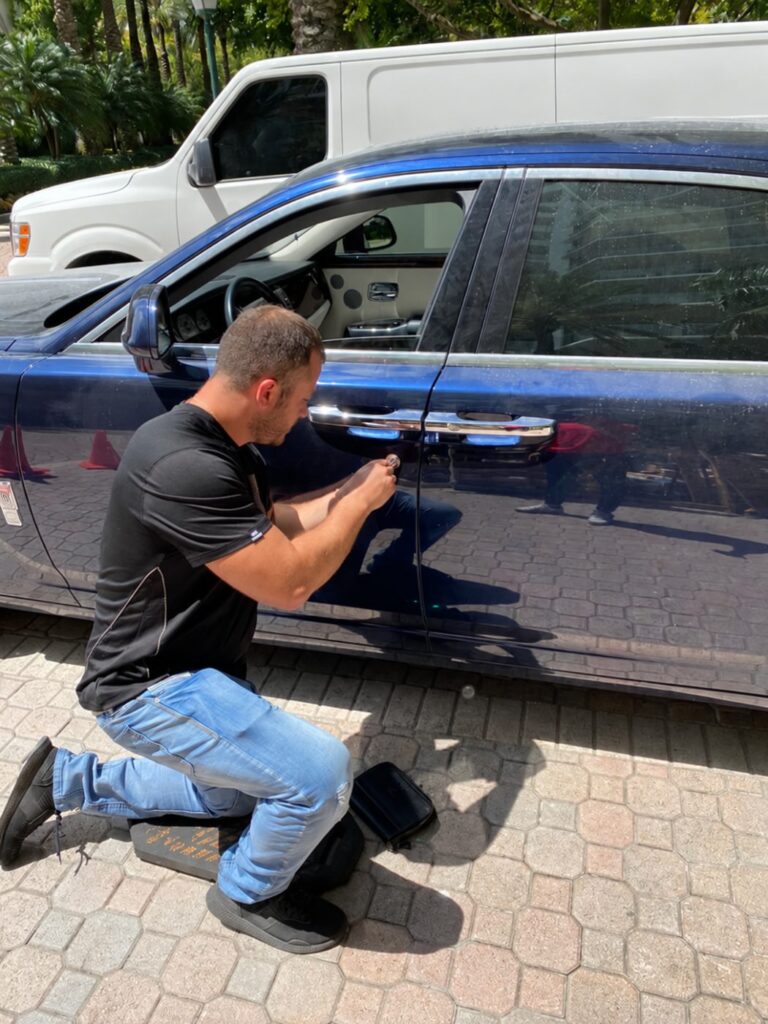 Locksmith opening the driver door of a luxury sedan during a car lockout call in Miami