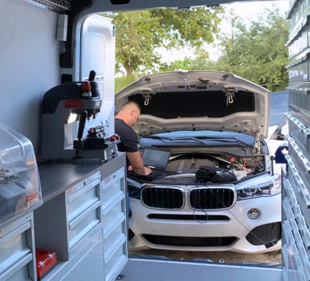 Mobile locksmith programming a BMW key with a diagnostic laptop beside a fully equipped service van in Miami