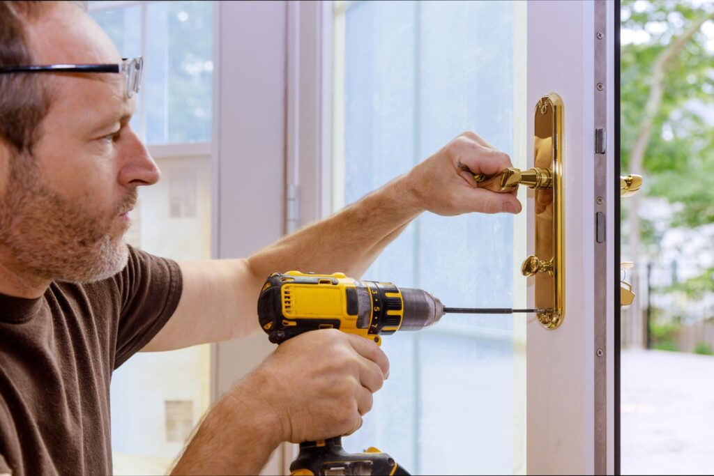 Residential locksmith installing a brass door handle and lock on a home entry door with a cordless drill